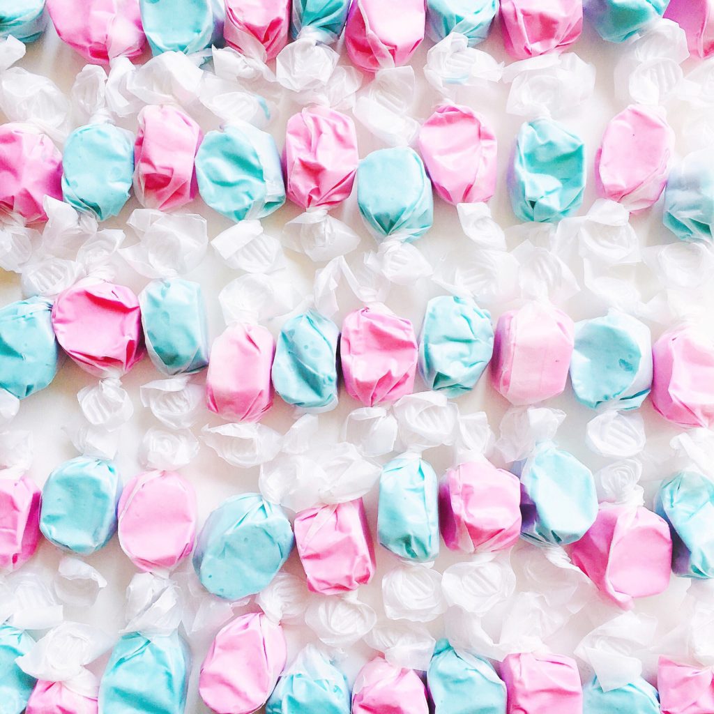 Neatly lined rows of wrapped alternating pattern pink and blue taffy candy on a white background.