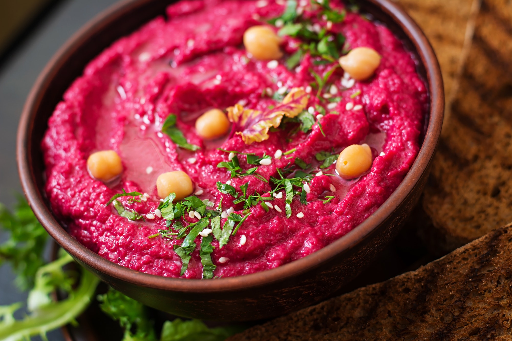 Roasted Beet Hummus with toast in a ceramic bowl on a dark background